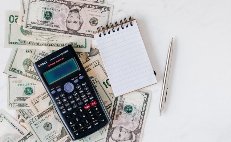 calculator and notepad placed over stack of usa dollars